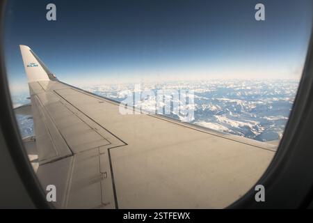 Une vue imprenable depuis la fenêtre passager d'un avion KLM, survolant des montagnes enneigées avec l'emblématique bout des ailes en vue. Banque D'Images