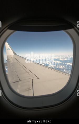 Une vue imprenable depuis la fenêtre passager d'un avion KLM, survolant des montagnes enneigées avec l'emblématique bout des ailes en vue. Banque D'Images