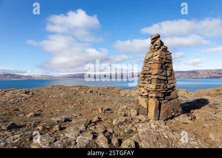 Cairn, tas de pierres artificielles faisant le sentier dans Westfjords, Islande, avec vue sur la mer et montagnes enneigées en arrière-plan. Banque D'Images