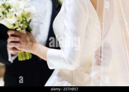 Mariée porte une robe blanche et tient un bouquet de fleurs. Un homme se tient derrière elle Banque D'Images