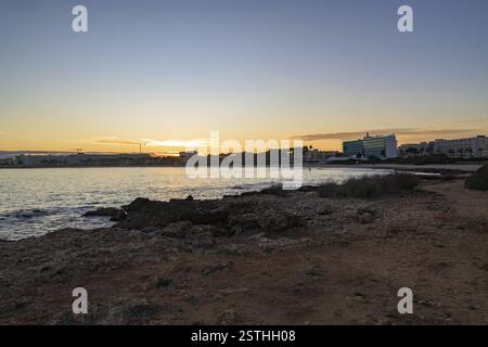 Coucher de soleil panoramique sur la côte rocheuse à Majorque, Espagne. La lumière dorée se reflète sur la mer calme, avec des bâtiments et des palmiers silhouettés dans le Banque D'Images
