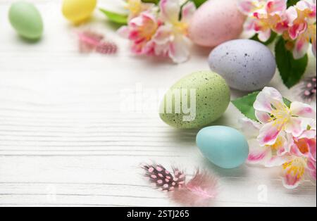 Œufs de pâques de couleur pastel et fleurs de printemps disposées sur des planches de bois blanc créant une bordure festive Banque D'Images