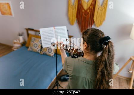 Jeune femme jouant du violon à la maison par partition, axée sur l'apprentissage de la musique Banque D'Images