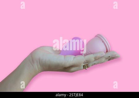 Coupe menstruelle en silicone rose et violet sur la main de la femme et isolé sur fond rose. Tasse hygiénique, espace de copie. Banque D'Images