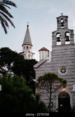 Église historique en pierre avec une façade rayée et un clocher. L'entrée voûtée est ornée de mosaïques religieuses, tandis que le clocher pointu et le lus Banque D'Images