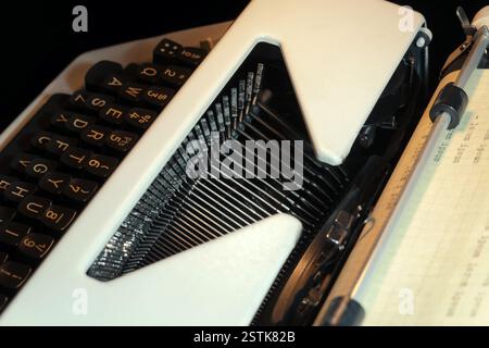Gros plan détaillé d'une machine à écrire ancienne avec des touches noires et des barres à caractères métalliques, avec un rouleau de papier chargé sur la platine. Idéal pour les thèmes de w Banque D'Images