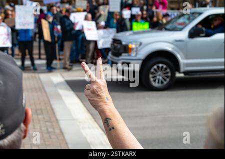 Une femme avec un tatouage d’espoir fait clignoter un signe de paix sur les voitures qui conduisent devant la manifestation « pas mon président » dans la rue devant le Capitole de l’État. Banque D'Images