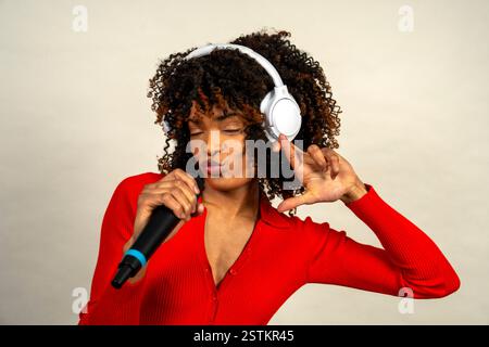 La jeune femme chante avec des écouteurs et un micro, profite de la musique et montre sa passion pour le chant Banque D'Images