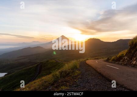 Un lever de soleil à couper le souffle sur une route de montagne sinueuse, entourée de vallées brumeuses et d'un ciel doré. Parfait pour les voyages, l'aventure et les thèmes de la nature. Banque D'Images