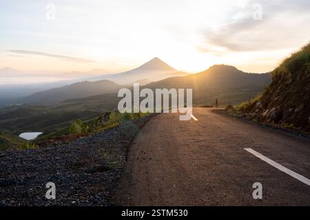 Un lever de soleil à couper le souffle sur une route de montagne sinueuse, entourée de vallées brumeuses et d'un ciel doré. Parfait pour les voyages, l'aventure et les thèmes de la nature. Banque D'Images
