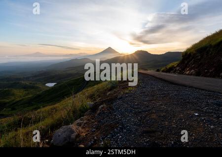 Un lever de soleil à couper le souffle sur une route de montagne sinueuse, entourée de vallées brumeuses et d'un ciel doré. Parfait pour les voyages, l'aventure et les thèmes de la nature. Banque D'Images