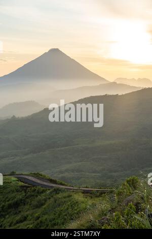 Un lever de soleil à couper le souffle sur une route de montagne sinueuse, entourée de vallées brumeuses et d'un ciel doré. Parfait pour les voyages, l'aventure et les thèmes de la nature. Banque D'Images