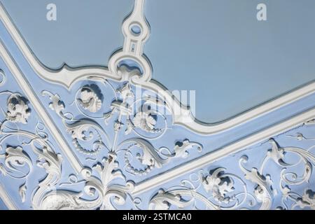 Moulure en plâtre sculptural blanc ornée avec des motifs et des motifs d'angle complexes sur un fond de plafond bleu clair, mettant en valeur le style classique Banque D'Images