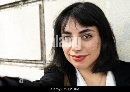 Confiante femme d'affaires hispanique en tenue classique sourit tout en prenant un selfie contre un mur blanc Banque D'Images