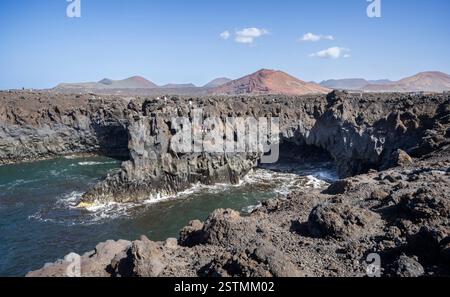 Le paysage volcanique de Los hervideros avec des vagues qui s'écrasent dans des grottes sous-marines et des cônes volcaniques en arrière-plan à Los Hervideros, Lanzarote, Espagne Banque D'Images