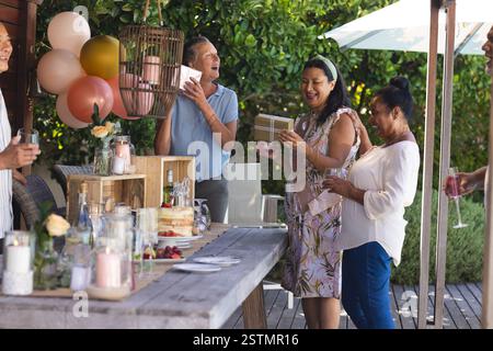 Échanger des cadeaux, divers amis seniors célébrant en plein air avec des rires et un rassemblement festif. Célébration, vacances, joie, ensemble, bonheur, Banque D'Images