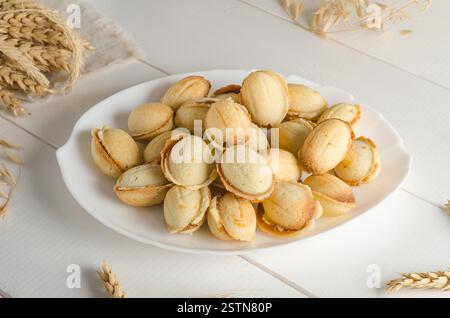 Délicieux biscuits sous la forme d'une noix remplie de lait condensé bouilli sur un fond en bois blanc. Banque D'Images