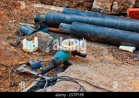 Meuleuse d'entraînement d'angle est couchée sur terre près d'un tas de tuyaux d'eau recouverts d'insylation de PVC Banque D'Images
