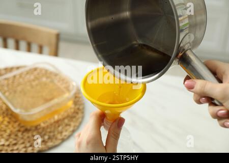 Femme versant de l'huile de cuisson usagée dans une bouteille à travers l'entonnoir dans la cuisine, gros plan Banque D'Images