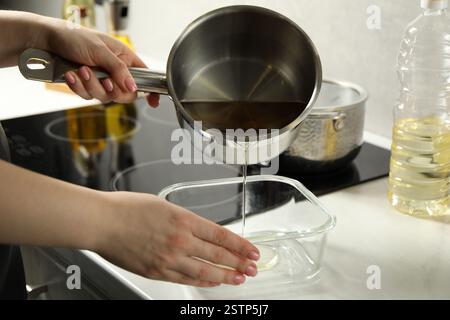 Femme versant l'huile de cuisson usagée dans un récipient en verre au comptoir en marbre blanc, gros plan Banque D'Images
