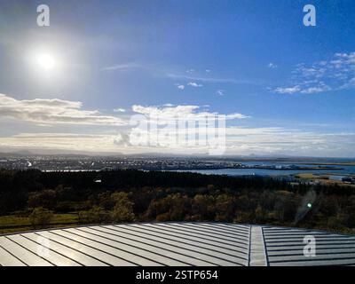 La photo capture une vue panoramique imprenable d'un paysage sous un ciel lumineux, avec un toit métallique en pente et une végétation luxuriante Banque D'Images