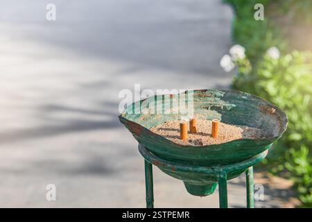 Trois mégots de cigarettes éteints dans le sable dans un vieux cendrier dehors par jour ensoleillé. Concept d'habitude nocive de fumer dans les lieux ouverts. Banque D'Images