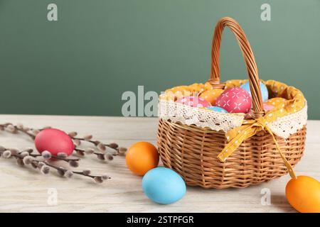 Beaucoup d'oeufs de Pâques décorés dans un panier en osier et des branches de saule sur une table en bois sur fond vert Banque D'Images