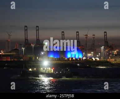 Hambourg, Allemagne. 19 février 2025. Les tours de digestion de la station d'épuration sont éclairées en bleu tandis qu'un navire navigue sur l'Elbe dans le port de Hambourg. Crédit : Marcus Brandt/dpa/Alamy Live News Banque D'Images