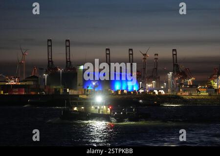 Hambourg, Allemagne. 19 février 2025. Les tours de digestion de la station d'épuration sont éclairées en bleu tandis qu'un navire navigue sur l'Elbe dans le port de Hambourg. Crédit : Marcus Brandt/dpa/Alamy Live News Banque D'Images