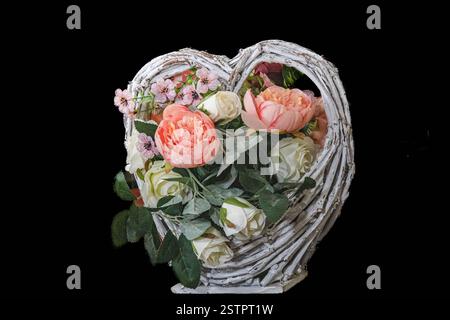 Panier en osier crème avec fleurs intemporelles, roses en papier crêpe, blanc et rose, avec feuilles vertes, sur fond noir Banque D'Images