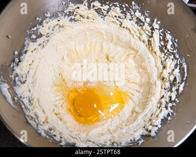 Battre le beurre, le sucre et les œufs dans un bol en métal gris. Le processus de fabrication de gâteaux et de biscuits en mélangeant du beurre, des œufs et du sucre. Gros plan d'un œuf en cr Banque D'Images