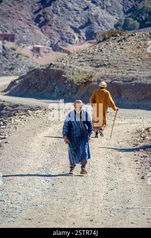 Deux hommes dans des kaftans marocains se croisent sur une route de montagne poussiéreuse dans les contreforts des montagnes de l'Atlas, au Maroc. Banque D'Images