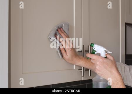 Femme nettoyant les armoires de cuisine avec un chiffon et un vaporisateur Banque D'Images
