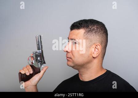 Photo stock d'un bel homme portant une chemise noire et un Jean tenant une arme à feu. isolé sur fond gris Banque D'Images