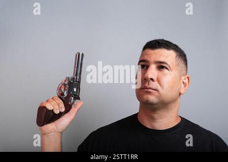 Photo stock d'un bel homme portant une chemise noire et un Jean tenant une arme à feu. isolé sur fond gris Banque D'Images