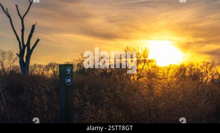 panneau de sentier pointant vers un coucher de soleil sur une prairie de campagne Banque D'Images