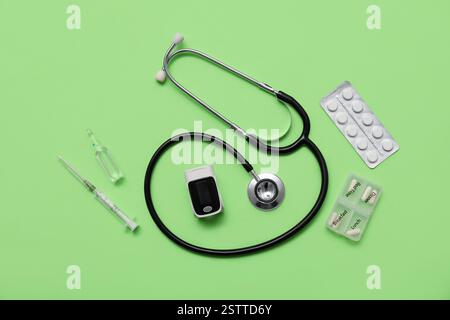 Oxymètre de pouls, ampoule, stéthoscope, pilules et seringue sur fond vert Banque D'Images