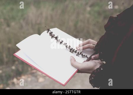 Une jeune femme tient un journal ouvert dans lequel une branche d'herbe est incrustée. Ambiance rétro Banque D'Images
