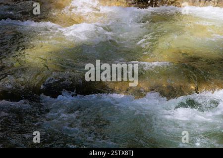 Une scène dynamique d'eau qui coule dans une rivière, mettant en valeur des teintes turquoise et vertes cristallines, avec des vagues mousseuses et des rochers submergés Banque D'Images