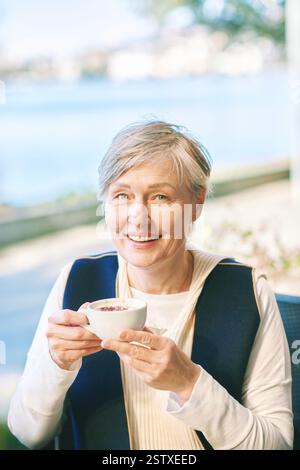 Portrait extérieur de la femme mature de 55 - 60 ans tenant une tasse de cappuccino Banque D'Images