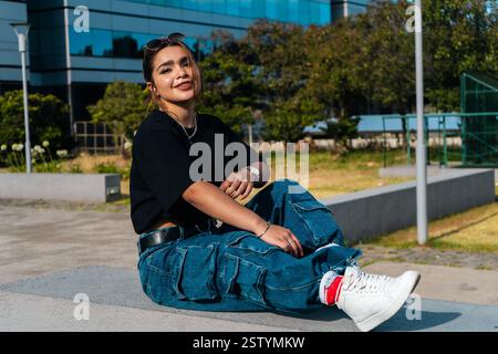 Jeune femme élégante profite d'un moment de détente dans un parc urbain moderne, affichant un style tendance et confiant Banque D'Images