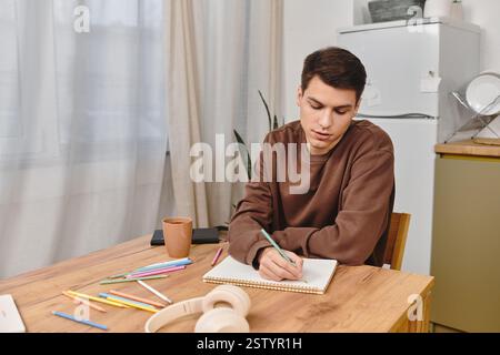 Un jeune homme est assis à une table en bois, concentré sur les croquis avec des crayons colorés. Banque D'Images