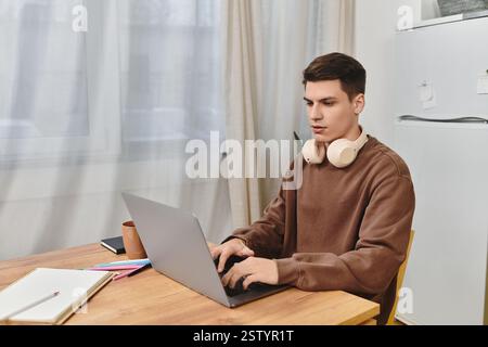 Jeune homme travaille intensément sur son ordinateur portable à une table en bois dans une maison confortable et confortable. Banque D'Images