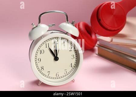 Réveil, livres et écouteurs sur fond rose clair Banque D'Images