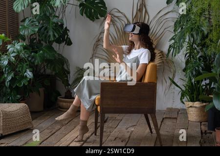 Une jeune femme portant un casque VR fait l'expérience de la réalité virtuelle pendant qu'elle se repose en serre Banque D'Images