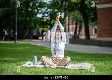Femme calme faisant du yoga de méditation sur la couverture sur la pelouse dans le parc. La fille s'étire, s'assoit en position lotus Banque D'Images