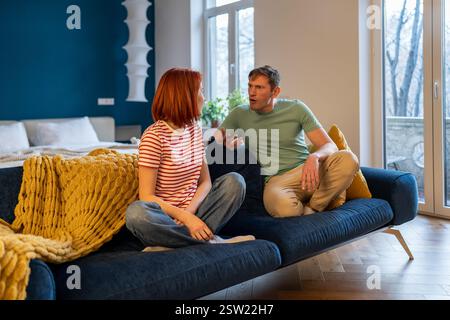 Relations toxiques agressif stressé violent tyran mari assis sur le canapé criant sur la femme. Banque D'Images