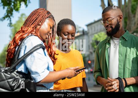 Heureux groupe d'amis africains discutant, femme avec le téléphone montrant le contenu des médias des fellows sur Internet Banque D'Images