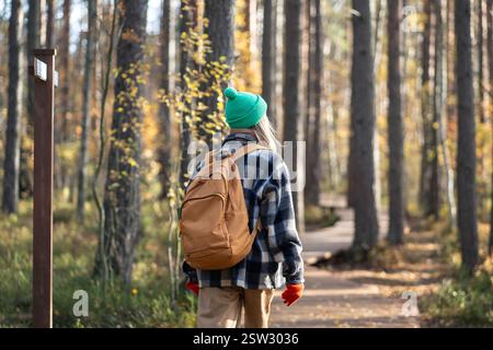 Femme touristique vue arrière avec sac à dos marchant sur le chemin écologique de la forêt le jour froid d'automne dans des vêtements chauds Banque D'Images