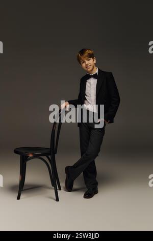 Vêtu d'un élégant smoking avec un noeud papillon, un garçon préadolescent pose en toute confiance dans un studio. Banque D'Images